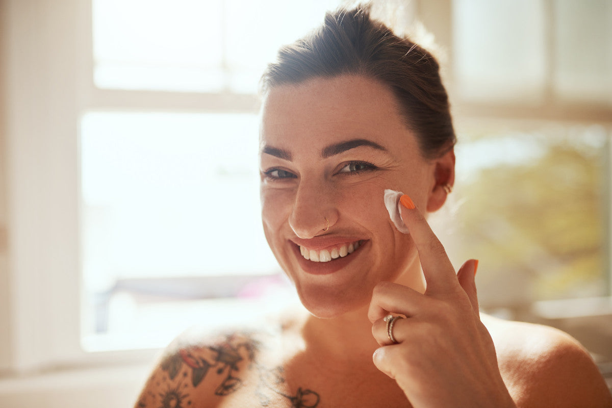 woman smiling, putting lotion on her cheek