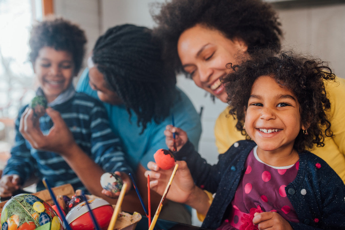 family smiling and painting Easter eggs together at the table