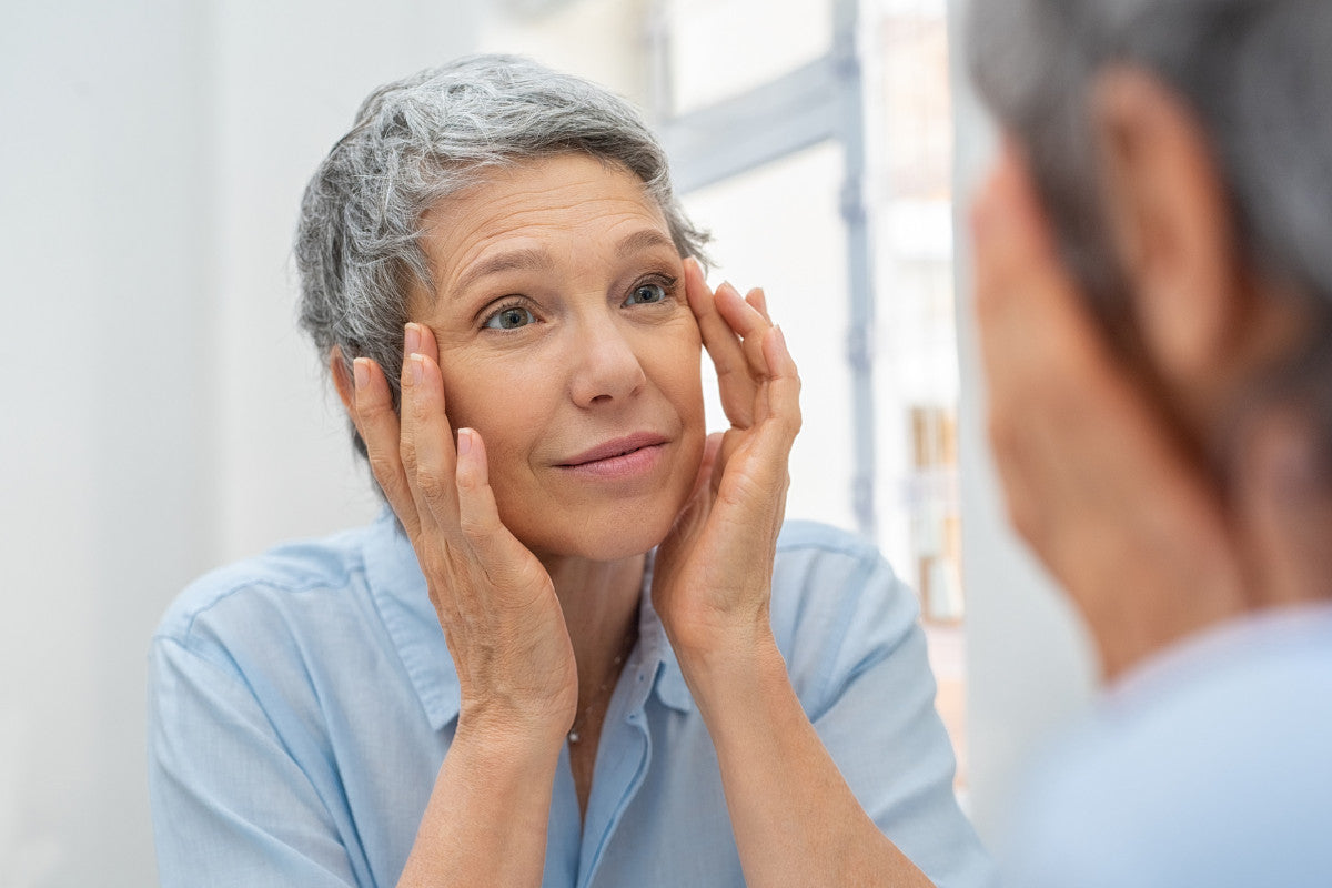 mature woman looking at herself in the mirror, with her hands on her face.