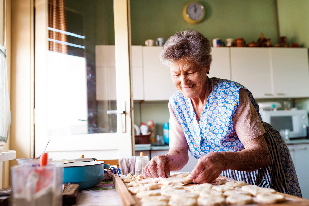 senior woman smiling as she places raw cookie dough on a baking sheet in her kitchen.