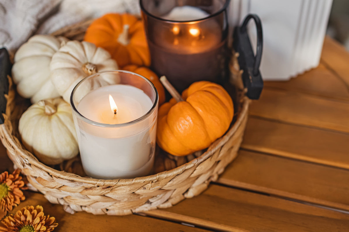 fall-scented candles and small white and orange pumpkins in a wicker basket.
