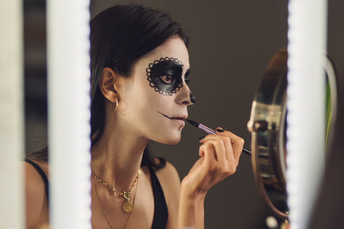 woman applying Halloween makeup over her lips while looking in a mirror