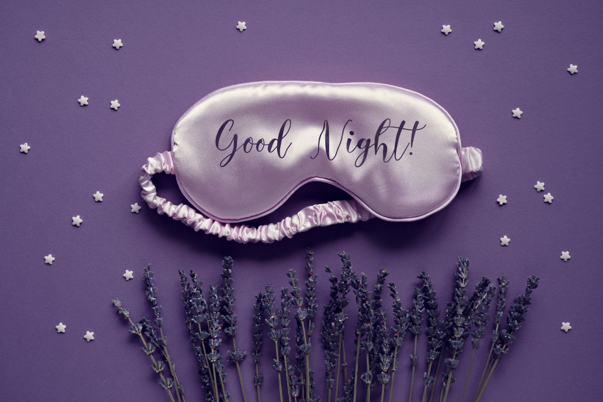 lavender sleep mask on a dark purple background that says
