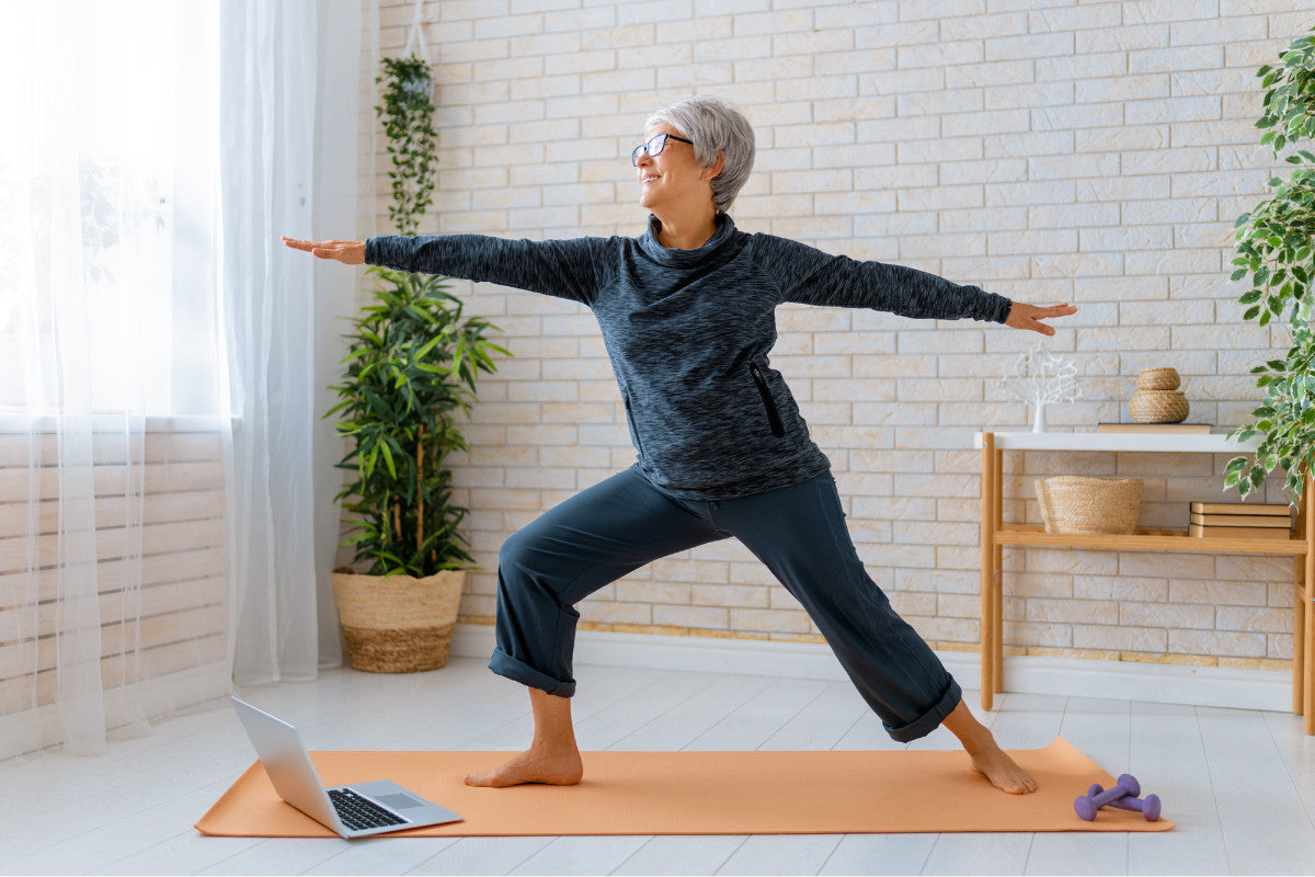 older woman smiling while practicing yoga in her home