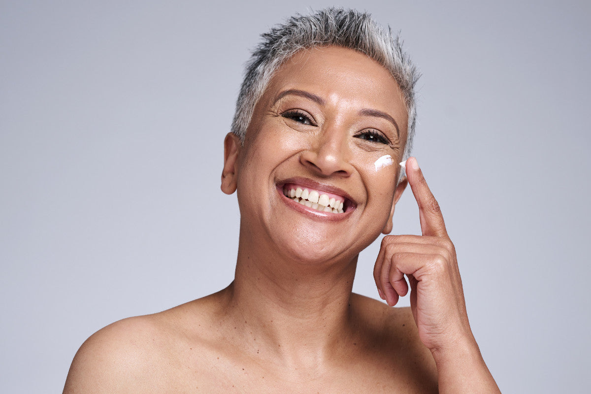 mature woman smiling, applying sunscreen to her cheek