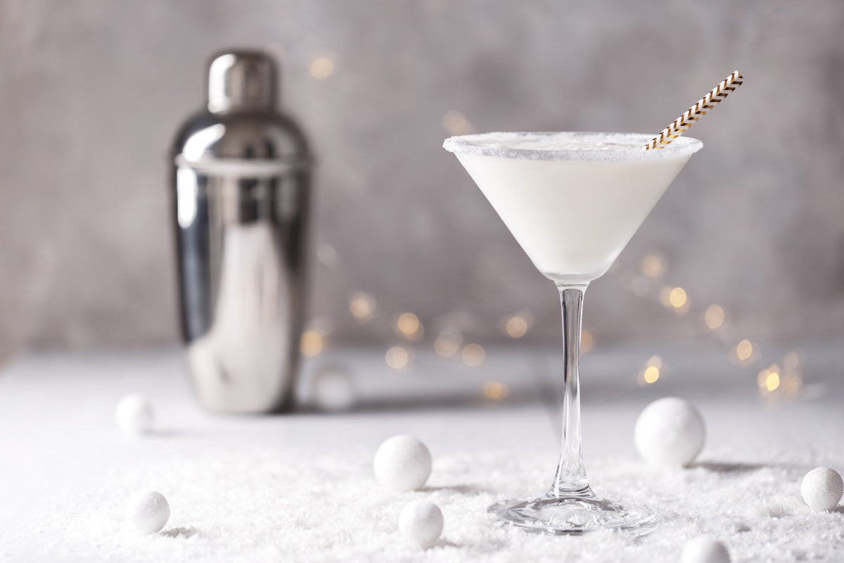 winter-themed cocktail and mixer sitting on top of snow with Christmas lights in the background