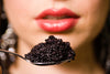 close up of spoon full of caviar in front of woman's mouth