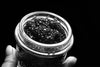 black and white photo of a hand holding up a jar of black caviar