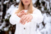 blurred woman wearing white coat outside in winter, holding up clear shot of moisturizing her hands