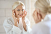 mature woman in bathrobe smiling in front of mirror, hands on her face