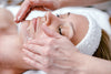 woman laying down in a spa while someone is putting a facial scrub on her
