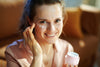 woman sitting on light brown couch, smiling as she puts on eye cream