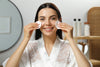 woman with glowing skin smiling, holding two cotton pads against both cheeks