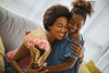 smiling child handing her smiling mother flowers as they both embrace each other