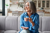 smiling older woman drinking a cup of coffee on the couch.