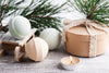 3 light-colored bathbombs sitting on a snowy wooden surface with pines in the back.