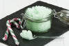 mint green body scrub in mason jar, sitting next to two wrapped red, white, and green candy canes.