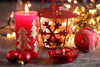 red candle with golden Christmas trees on it, sitting next to a red snowflake lantern and some red ornaments.