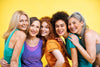 group of women with different ages, ethnicities, and body types, all standing together and smiling on a yellow background