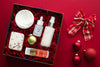 various skincare items in a red box with holiday ornaments and a plaid red and white ribbon to the right of it.