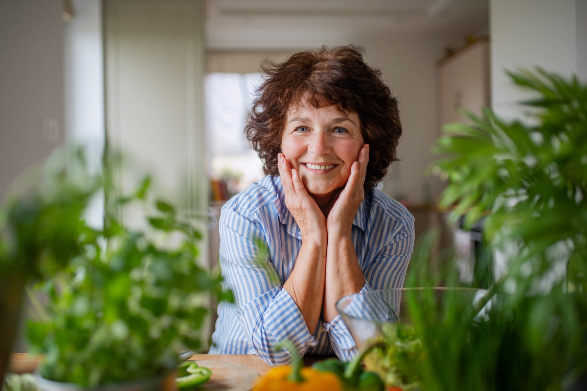Senior woman smiling inbetween plants.