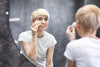 mature woman using a cotton pad to apply skincare products while looking in the mirror