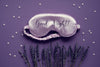 lavender sleep mask on a dark purple background that says 