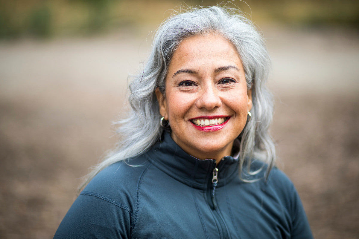 older woman smiling. standing outside wearing a gray-blue jacket.