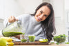 woman smiling as she pours a green smoothie into two glass cups