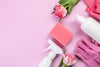 light pink background with generic white cleaning bottles, pink rubber gloves, a pink sponge, and pink roses.