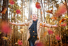 Mature woman in autumn forest, dressed in cozy fall attire, smiling and embracing the falling leaves.