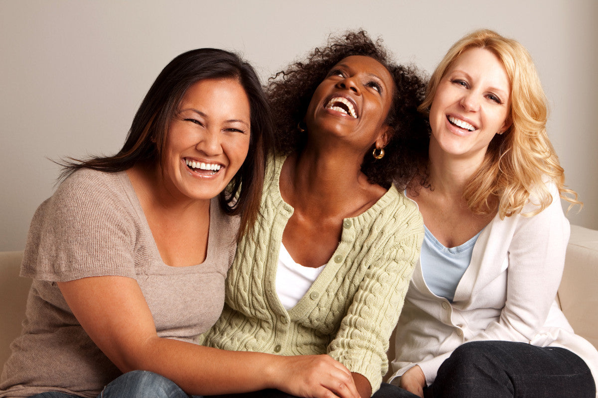 three mature women sitting on a couch and laughing together