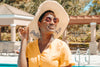 woman wearing a yellow shirt, sun hat, and sunglasses, smiling and enjoying the sun by the pool