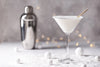 winter-themed cocktail and mixer sitting on top of snow with Christmas lights in the background